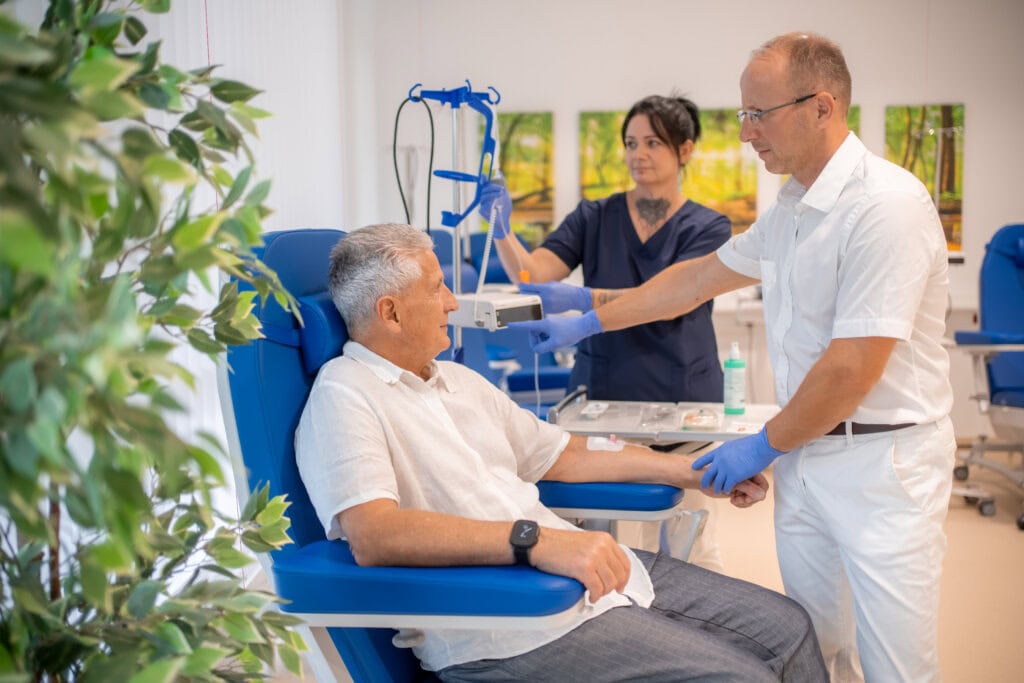Patient sitzt auf einem Untersuchungsstuhl und wird von Arzt und MFA versorgt